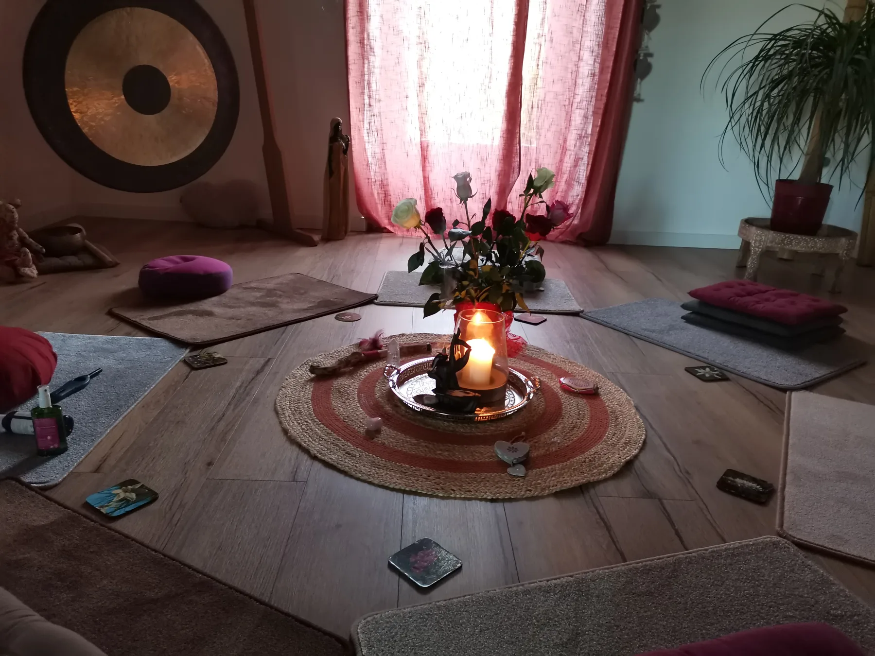 Salle de pratique, tapis et coussins en cercle autour d’une bougie et d’un bouquet, un gong dans l’angle