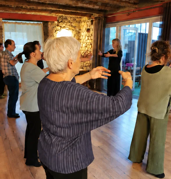 Cours de Qi Gong dans la salle aux murs de pierre, Catherine face au groupe, bras ouverts