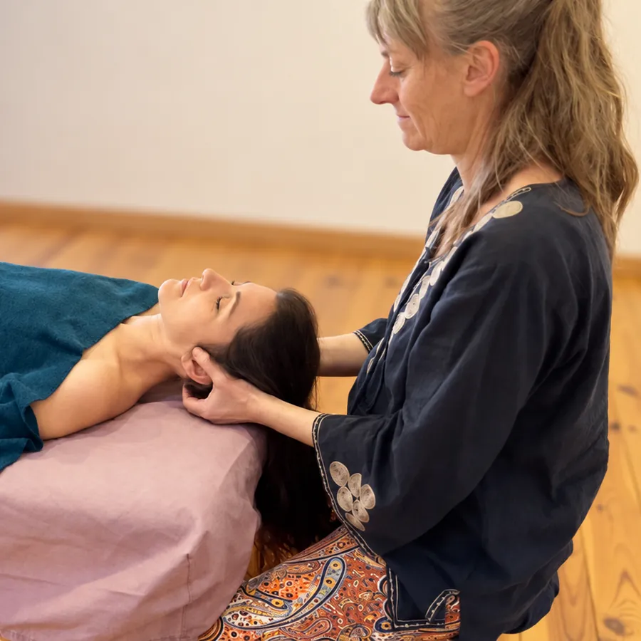Un massage de la tête : la praticienne, à genoux, soutient la tête d’une personne allongée