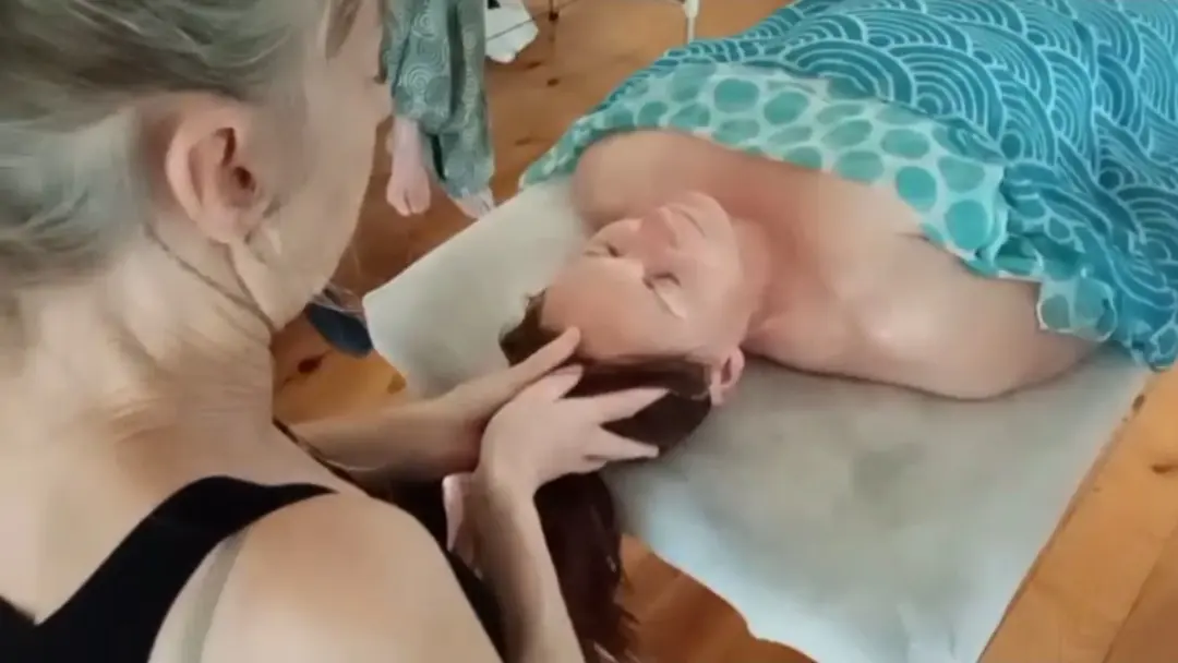 Un soin crânien : les mains de la praticienne soutiennent la tête d’une personne allongée